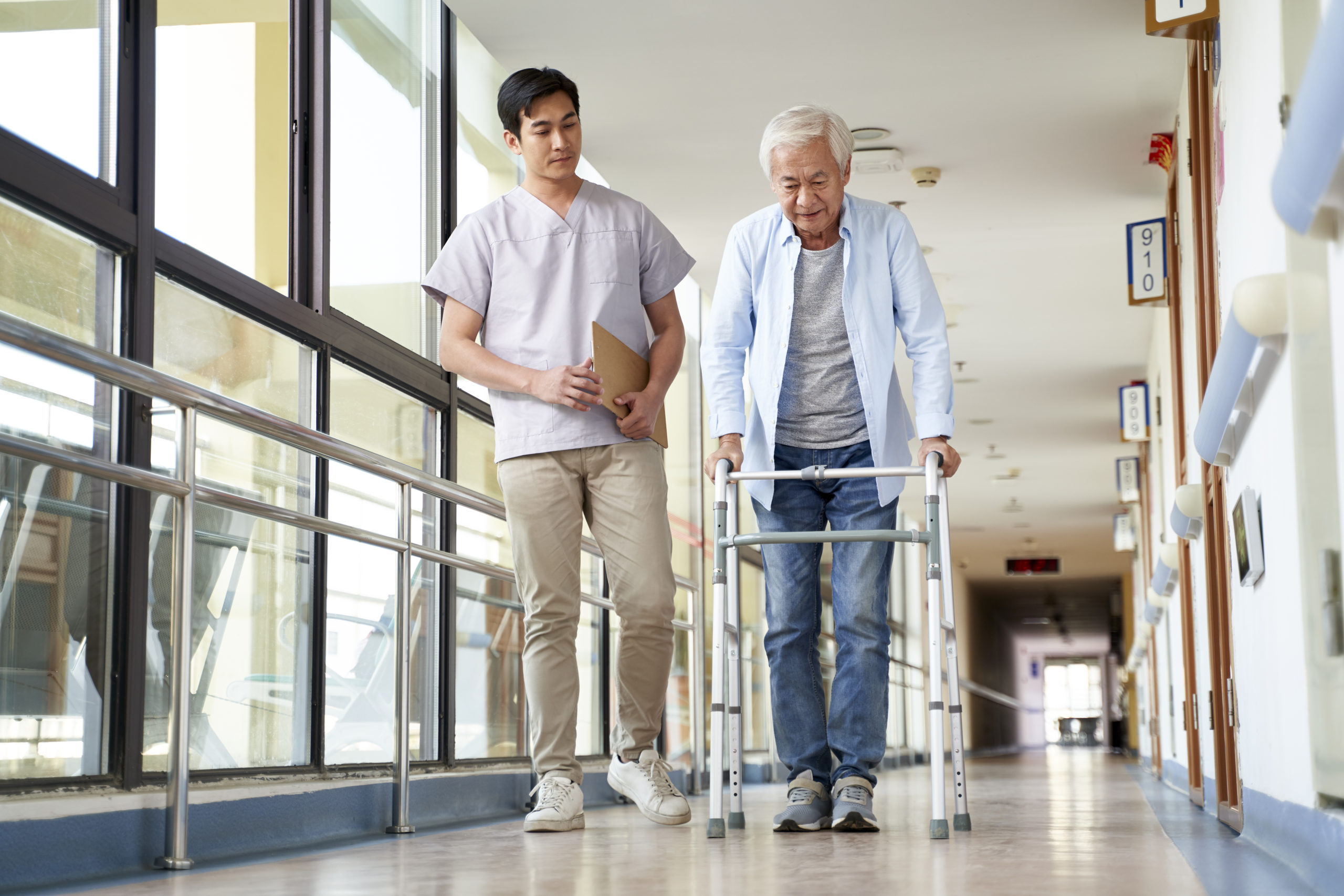 young asian physical therapist working with senior man on walking using a walker